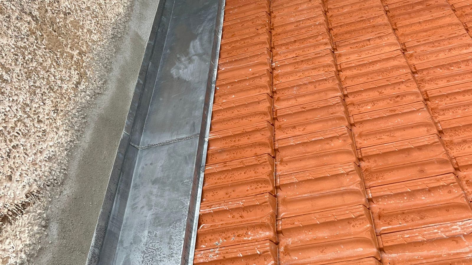 Chéneau en zinc le long d'un mur crépi, au bas d'un versant en tuiles neuves